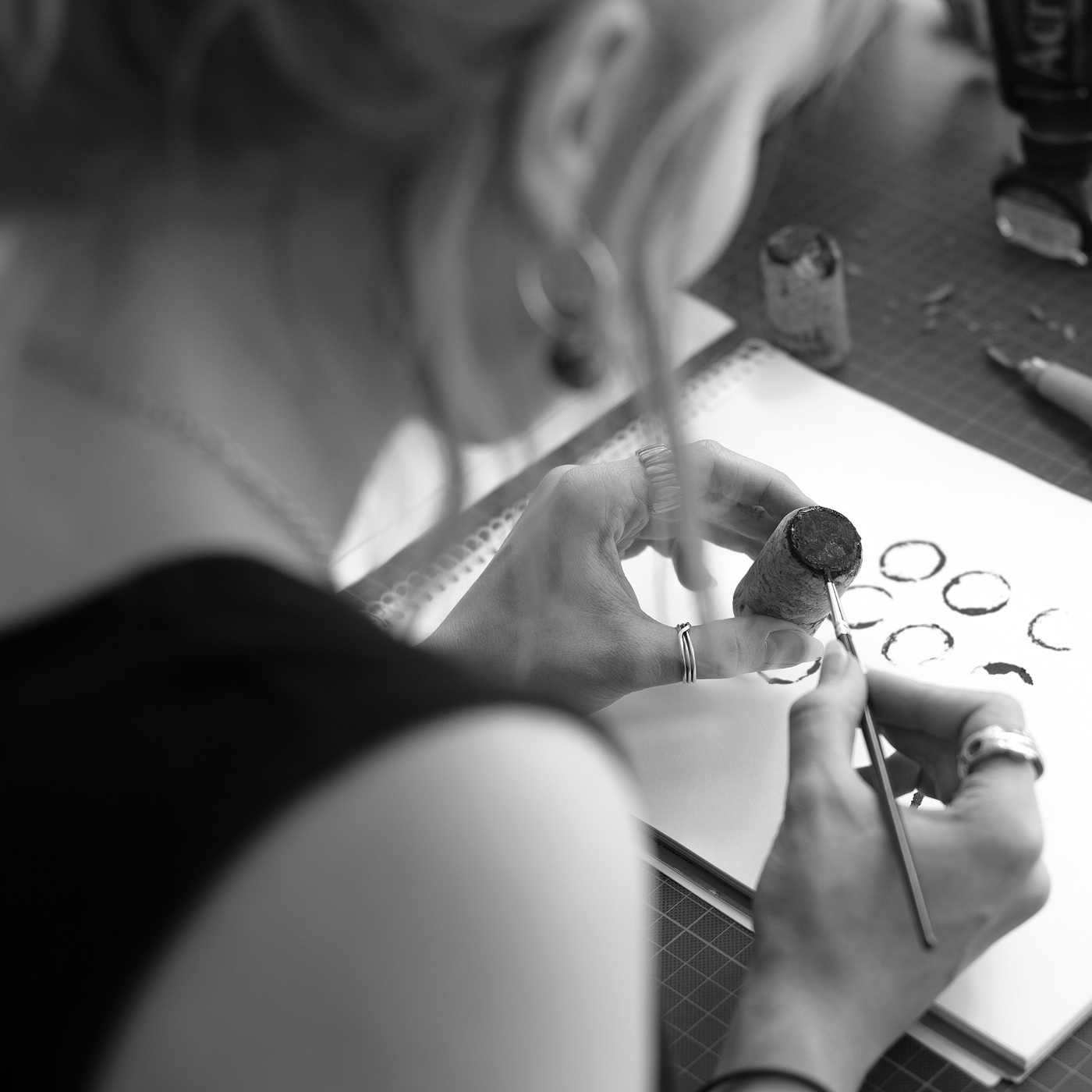 Person bemalt einen Korken-Stempel und druckt runde Formen in ein Skizzenbuch auf einem Arbeitstisch.