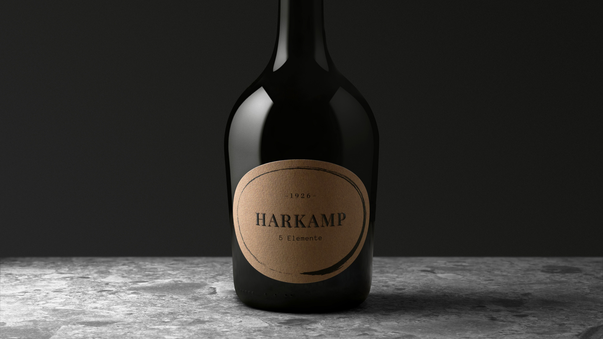 Detailaufnahme einer dunklen Flasche mit rundem Etikett „HARKAMP 5 Elemente“ auf steinartiger Oberfläche.