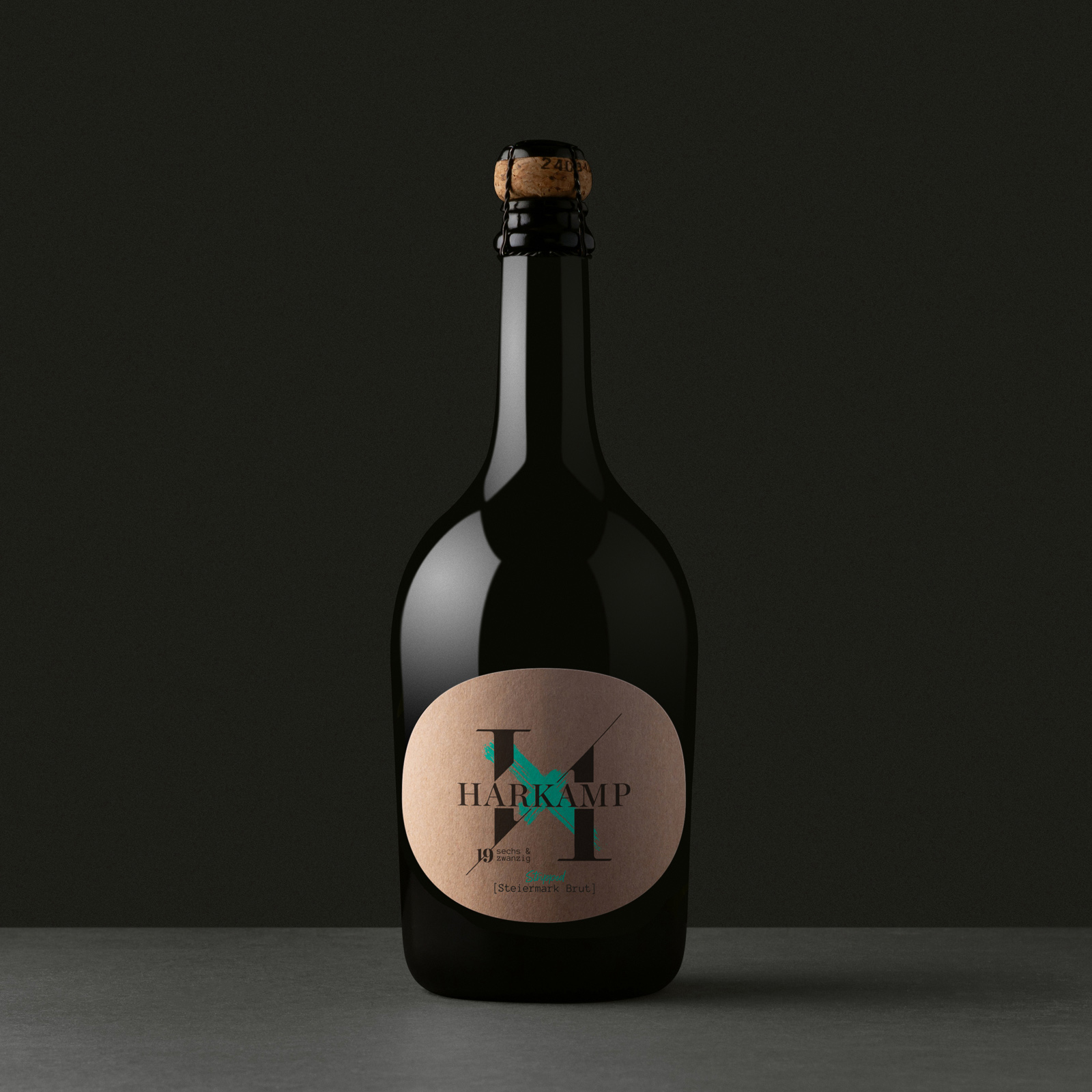 Dunkle Sektflasche mit rundem Etikett „HARKAMP Steiermark Brut“ und großem H-Motiv auf dunklem Hintergrund.