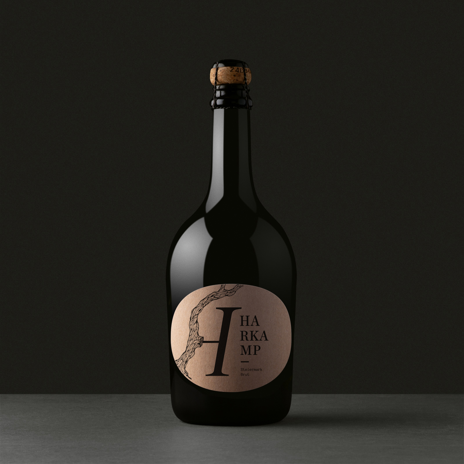 Dunkle Sektflasche mit rundem Etikett, großem „H“-Motiv und feiner Linienillustration auf dunklem Hintergrund.