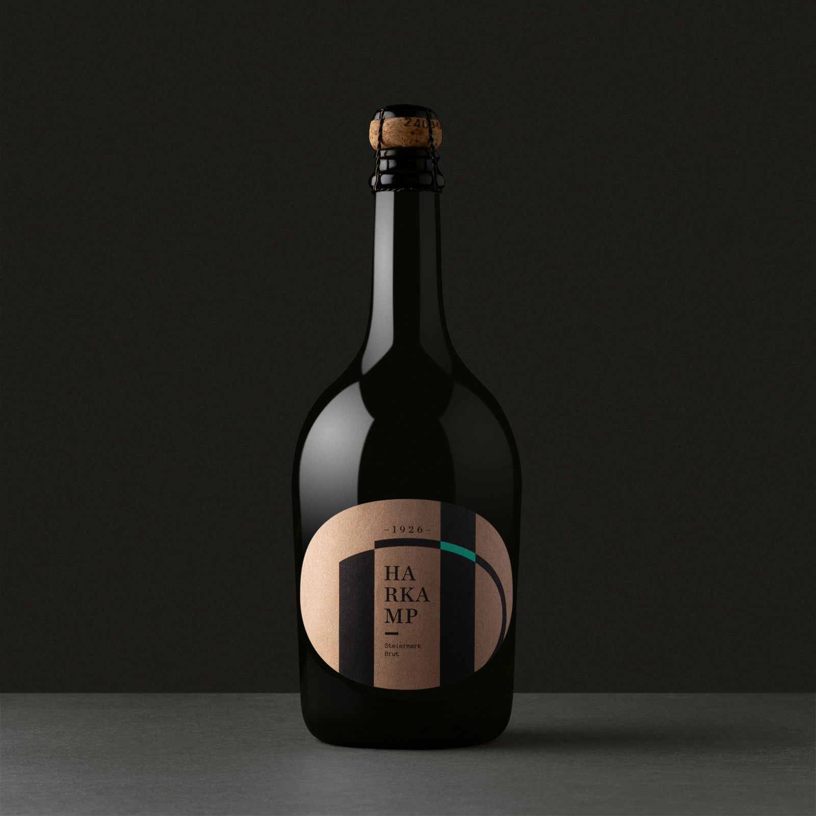 Dunkle Sektflasche mit rundem Etikett, schwarzen Streifen und grünem Bogen-Element vor dunklem Hintergrund.